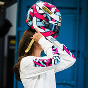 A person wearing a Hoonigan x Lia Block SCRIPT Long Sleeve T-Shirt holds a colorful helmet, showcasing motorsport culture.