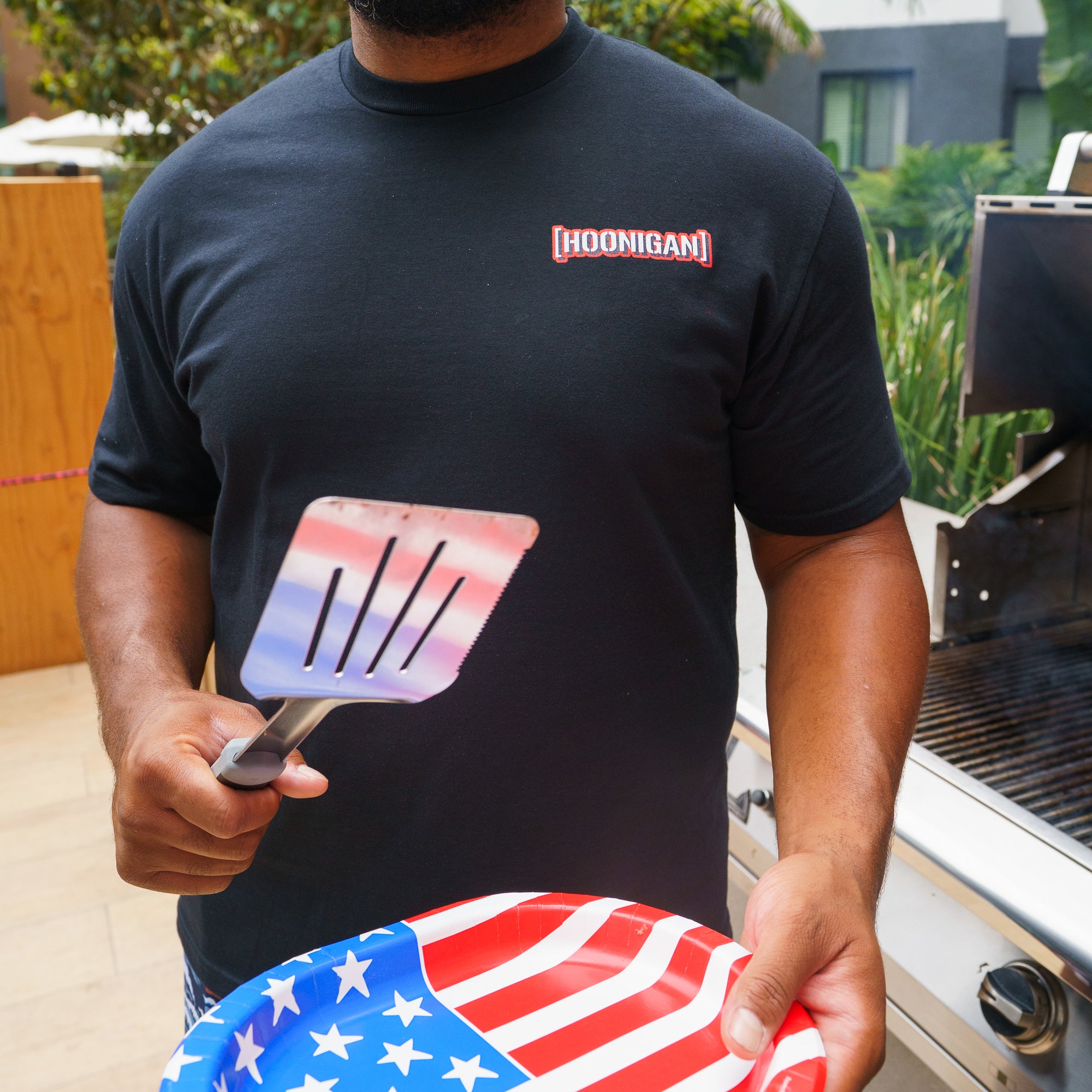 Black Hoonigan KILL ALL TIRES USA short sleeve T-shirt with red and white logo on the chest, held by a person outdoors.