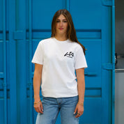Model wearing a white Hoonigan x Lia Block H BOX short sleeve t-shirt against a blue background, showcasing automotive lifestyle apparel.