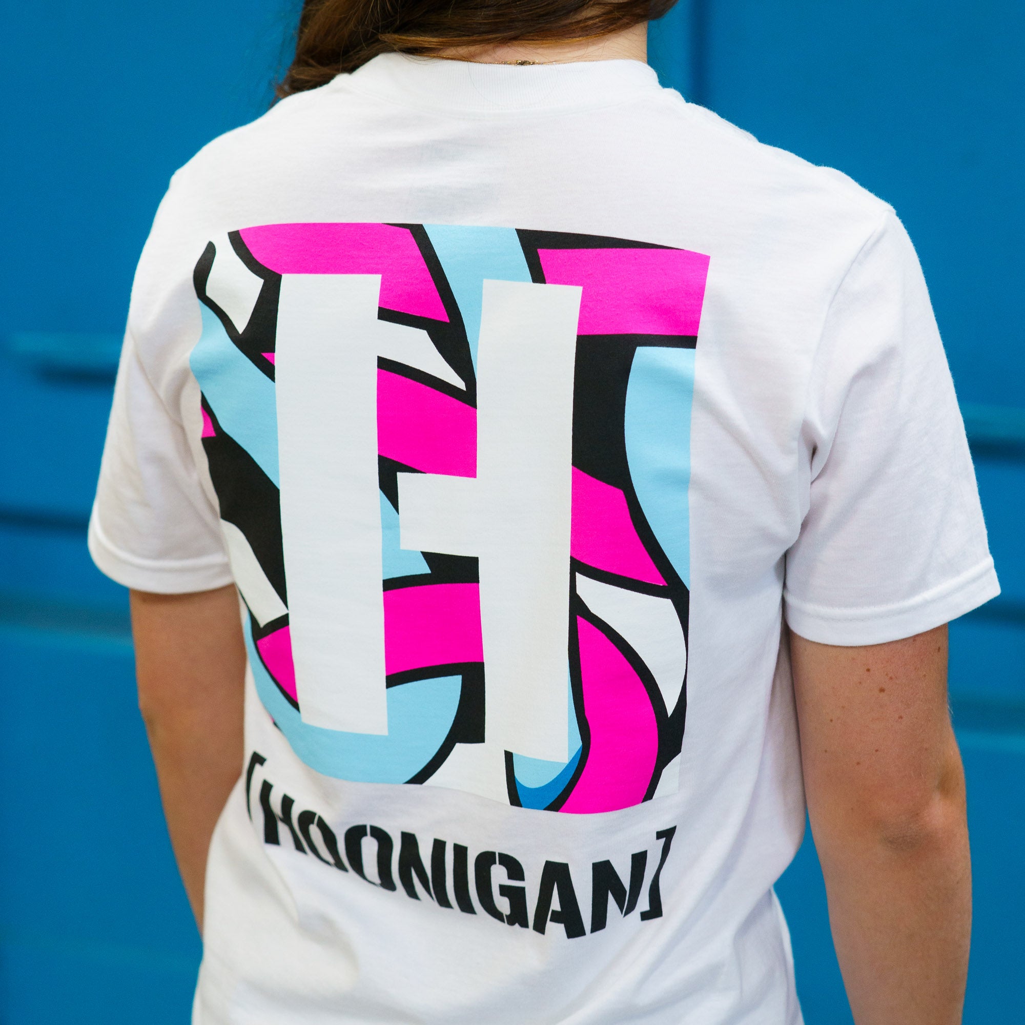White short sleeve t-shirt featuring a bold Hoonigan logo in vibrant colors on the back, perfect for motorsport enthusiasts.