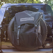 Hoonigan CENSOR BAR spare tire backpack attached to a vehicle, designed for motorsport enthusiasts and outdoor adventures.