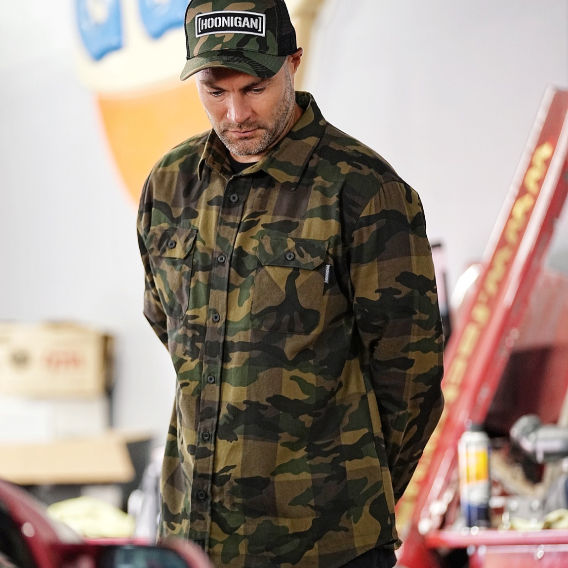 Hoonigan H Icon Camo Woven Flannel Long Sleeve Shirt featuring a camo pattern and Hoonigan logo, displayed on a wooden background.