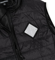 Close-up of a black GRILLE Puffer Vest with horizontal quilting, zipper closure, and a diamond-shaped patch on the chest.