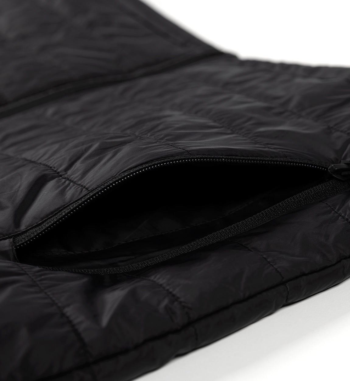 Close-up of a black GRILLE puffer vest with a zipper pocket, showcasing quilted, shiny, lightweight, insulated material.