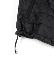Close-up of a black GRILLE puffer vest showing quilted fabric, a zippered pocket, and an adjustable drawstring at the hem.